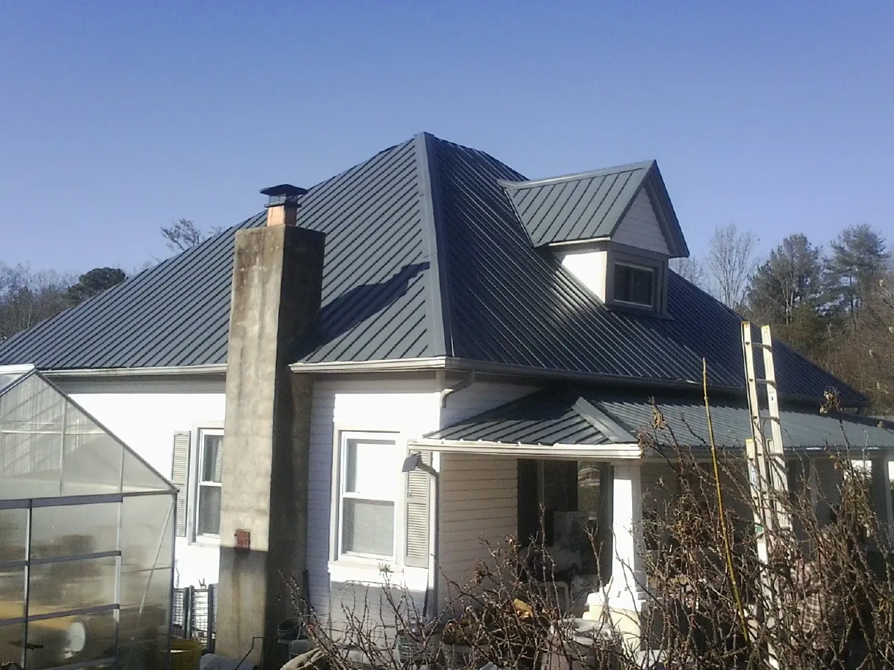 Dark blue standing seam metal roof on a white farmhouse with dormer — Slate & Tile Roof Repair by Roofing Brothers in Larimer