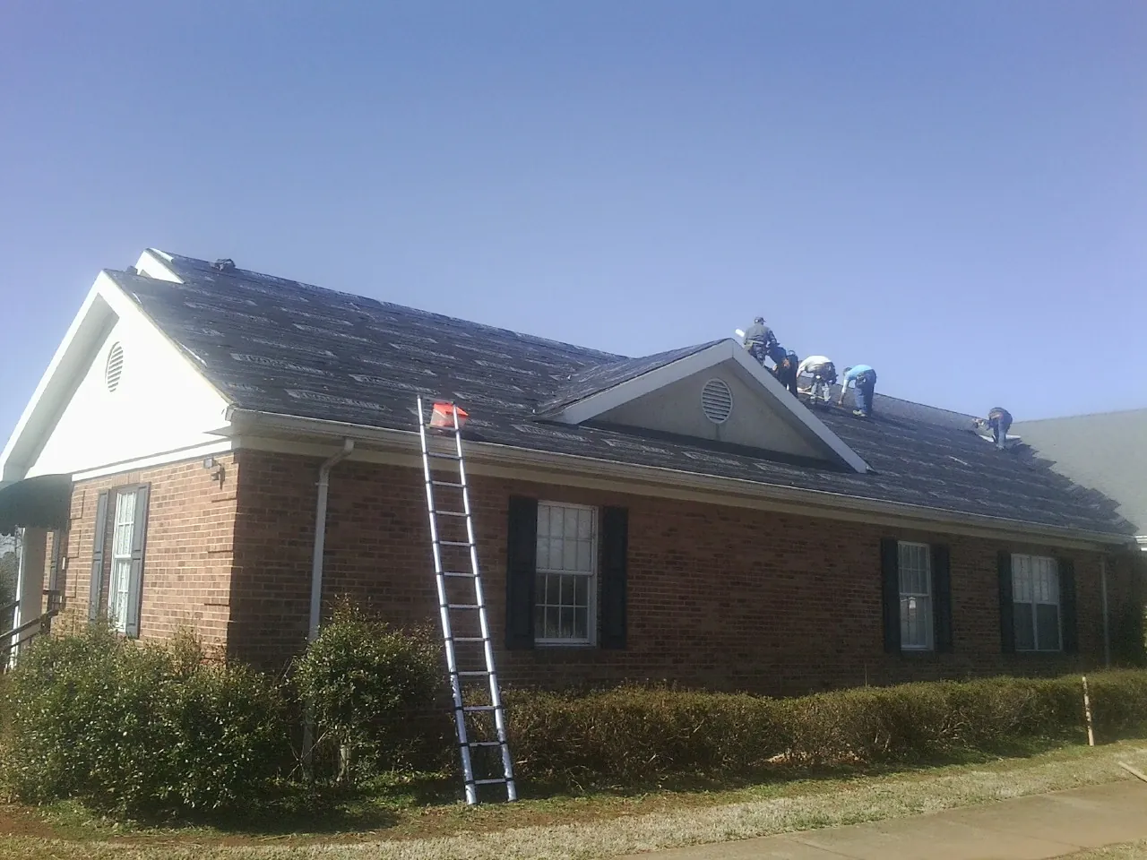 Crew tearing shingles off a brick ranch roof with a ladder set — Emergency Roof Repair work by our crew in Larimer