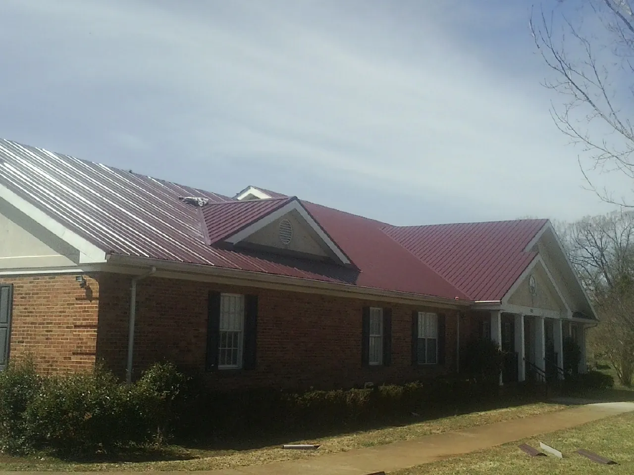 Red metal roof with gabled entries on a long brick building, from a Hail Damage Roof Repair job in Larimer
