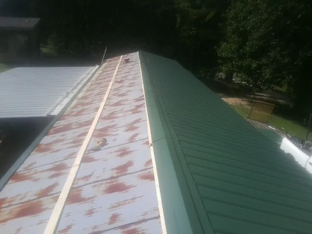 Old rusted panels beside newly installed green metal roofing — Wind Damage Roof Repair by Roofing Brothers in Larimer