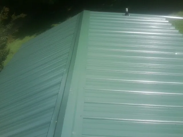 New green metal panels meeting at the ridge of a roof — Flat Roof Repair work by our crew in Larimer