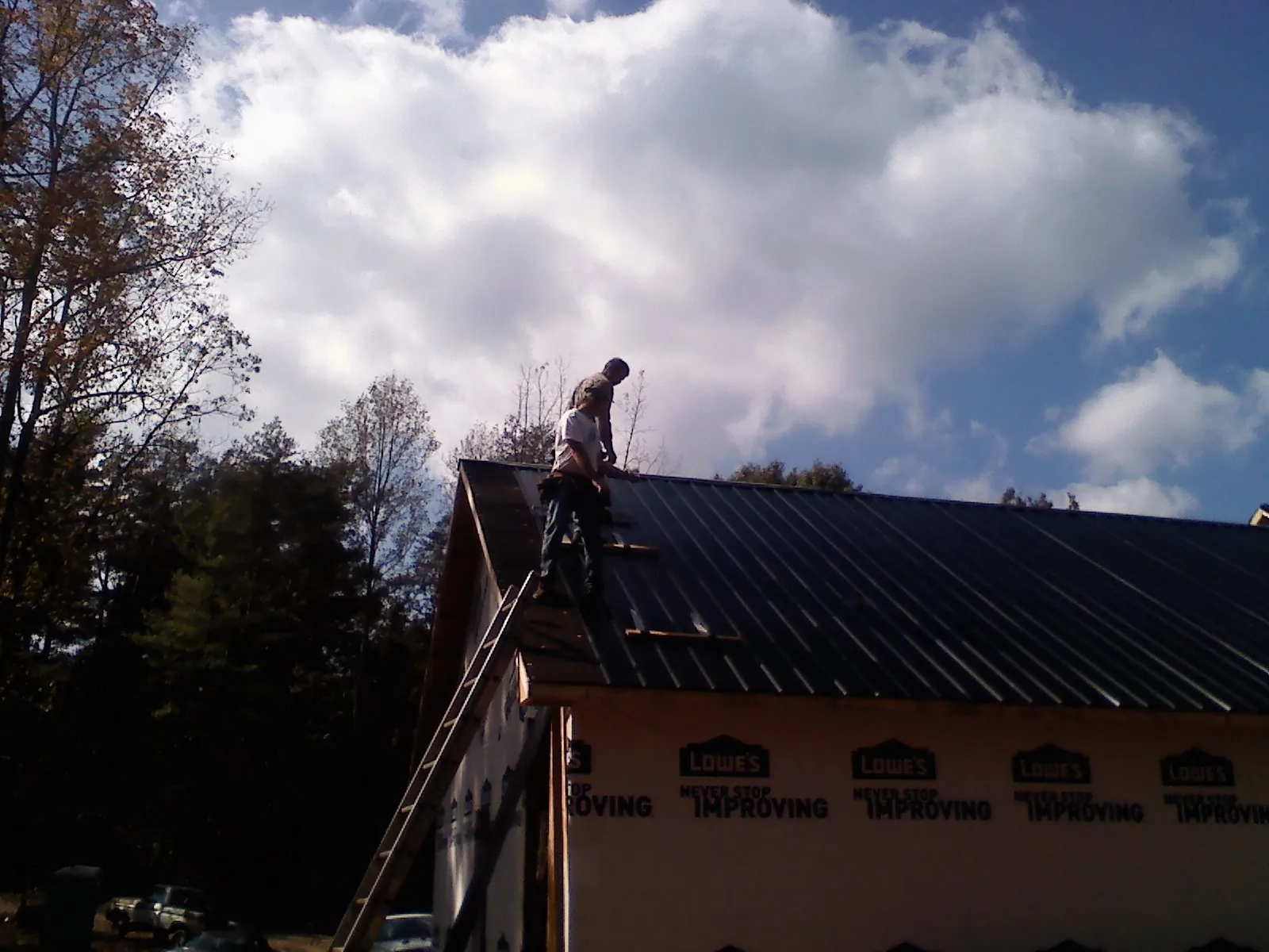 Roofer fastening dark metal panels high against a cloudy sky, from a Roof Inspection job in Larimer