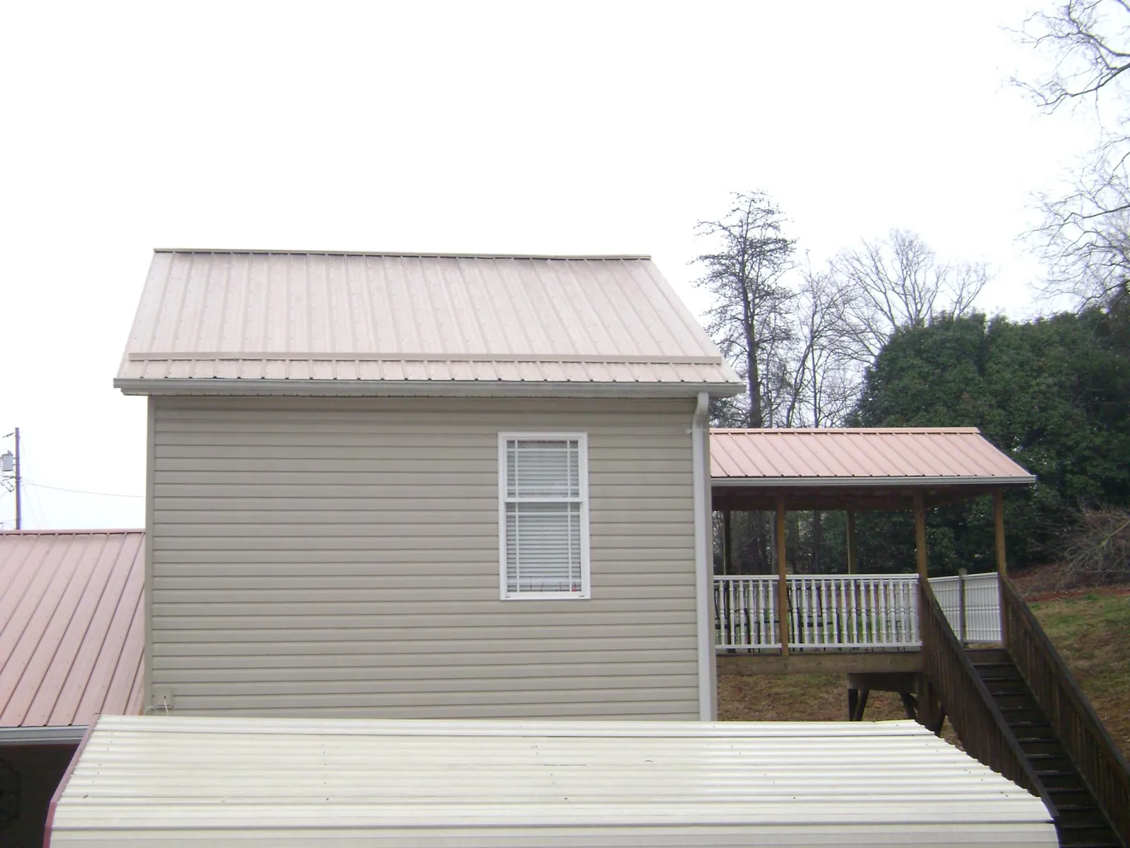 Tan metal roofs on a two story addition and attached porch, from a Roof Replacement job in Larimer